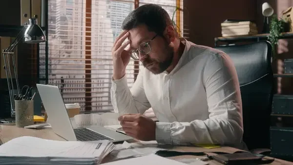 Mann sitzt am Laptop im Büro und wirkt gestresst