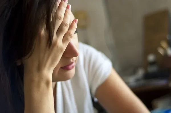 Frau stützt ihr Gesicht in ihre Hände und leidet offenbar an chronischer Erschöpfung, sie sieht sehr müde aus.